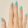 Hand with teal turquoise glittery LED gel strips on nails on a beige background