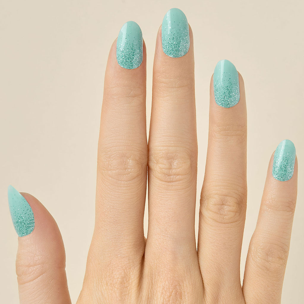 Hand with teal turquoise glittery LED gel strips on nails on a beige background