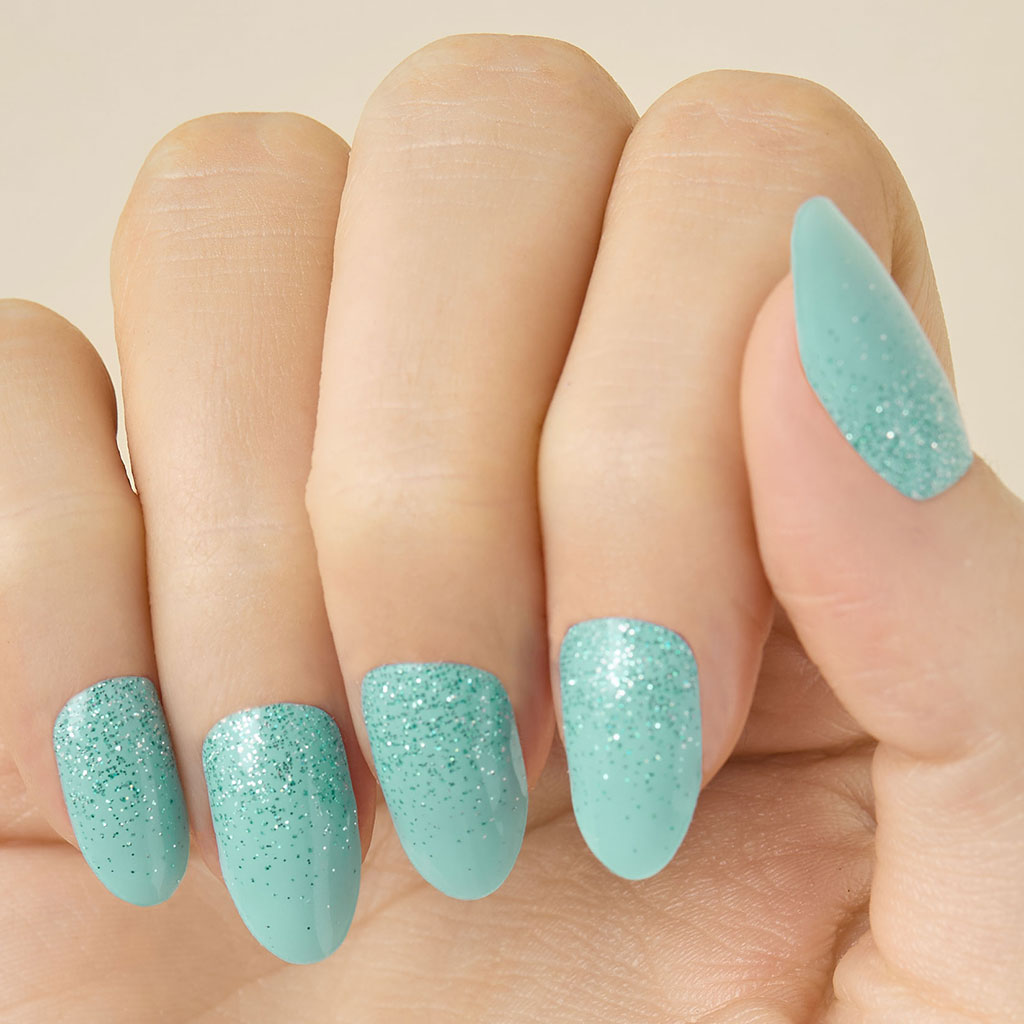 Close- up of a hand with teal turquoise glittery LED gel strips on nails on a beige background