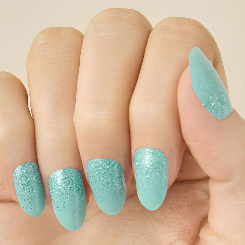 Close- up of a hand with teal turquoise glittery LED gel strips on nails on a beige background