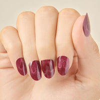 Closeup of hand with glittery red burgundy heart magnetic valentine day LED gel strip nails on a beige background