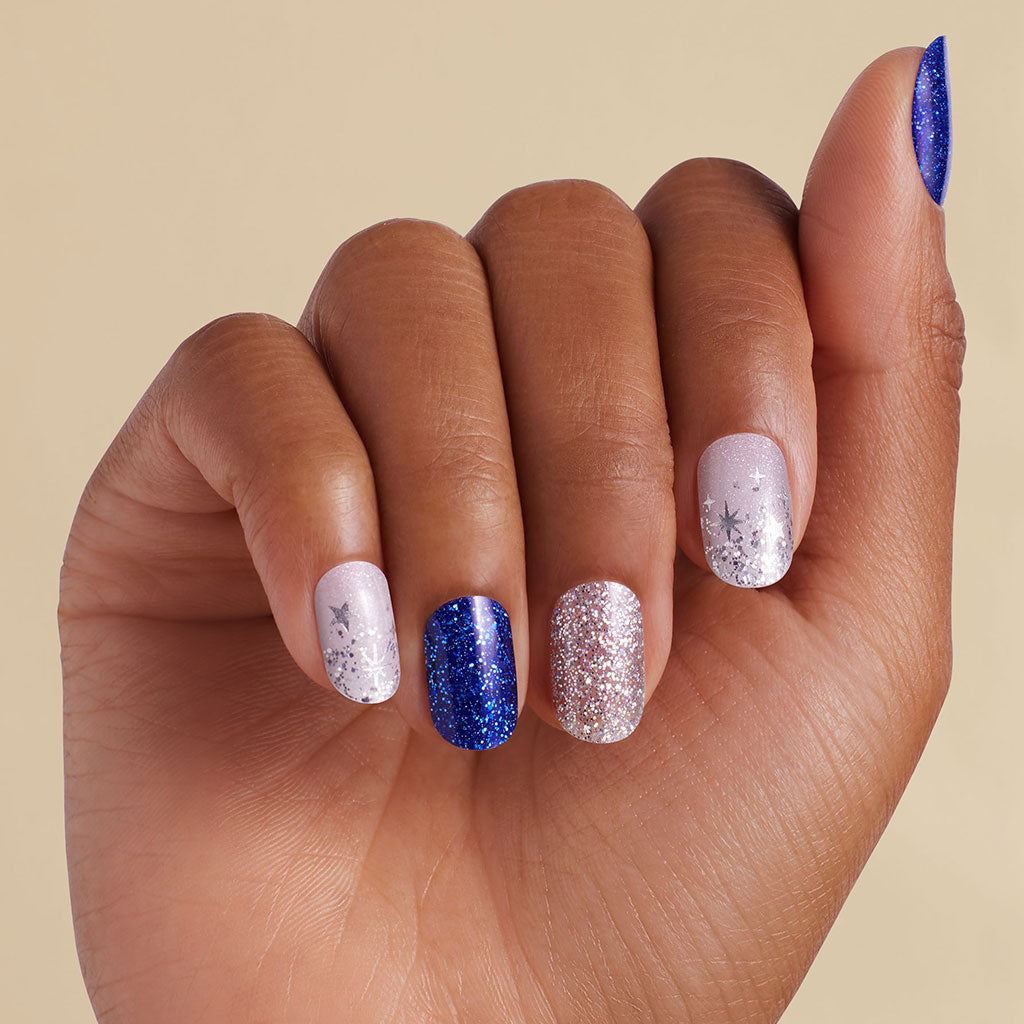 Hand with blue and silver glitter LED gel strip nails on beige background