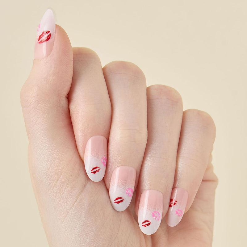 Closeup of hand with ombre press on nails and red lip print on a beige background