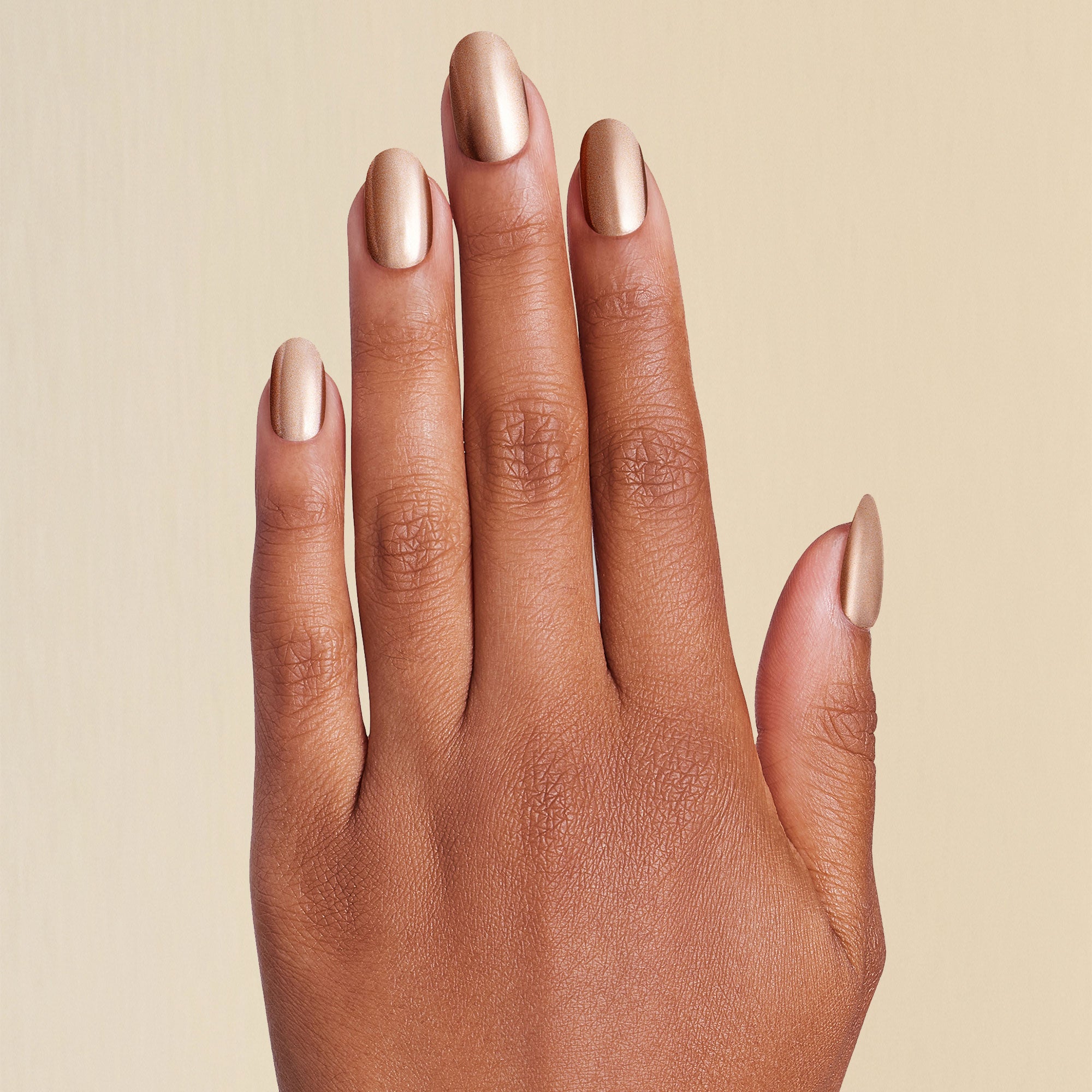Hand with press on gold chrome short round nails on beige background